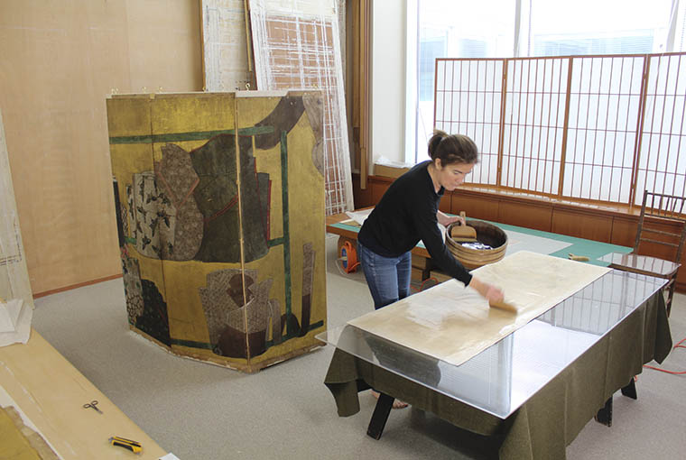 A conservator applying a wheat starch paste to a Japanese folding screen
