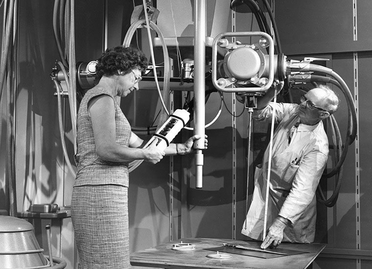 Two conservators setting a painting in a very large X-ray machine for radiographing materials
