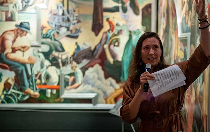 A fellow holds a mic and gives a presentation in a gallery