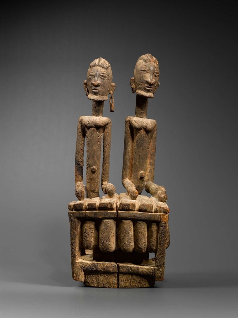A sculptural object depicting two musicians standing side-by-side playing a xylophone-like bala.