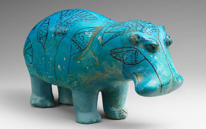 A blue ceramic hippopotamus with lotus flower details on its trunk, facing right. 