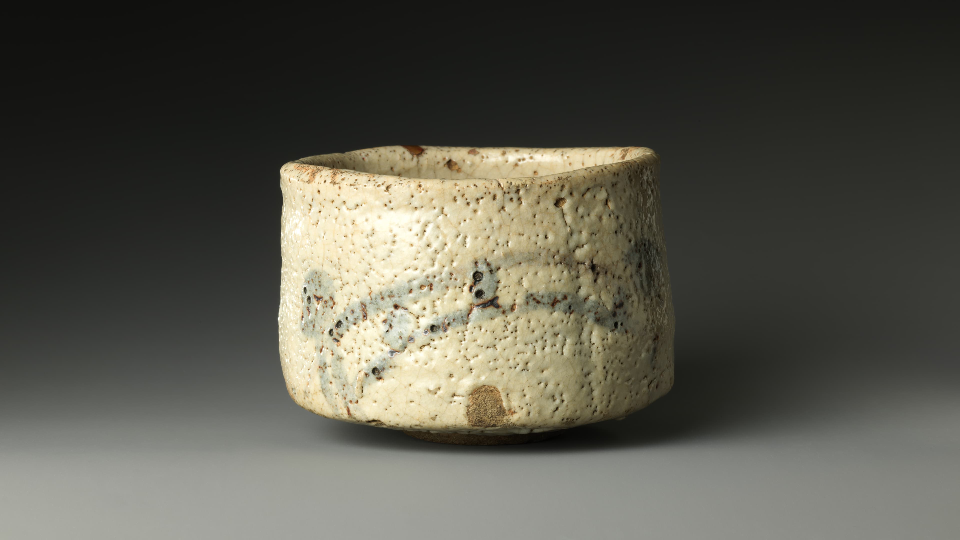 A white-glazed tea bowl depicting, in brown, an arching bridge on the front and a Shinto shrine on the back. The thick, white glaze on top of brown iron oxide creates the impression of a mist-shrouded landscape. Under the bridge, a fingerprint marks the spot where the potter held the bowl while dipping it into the glaze.