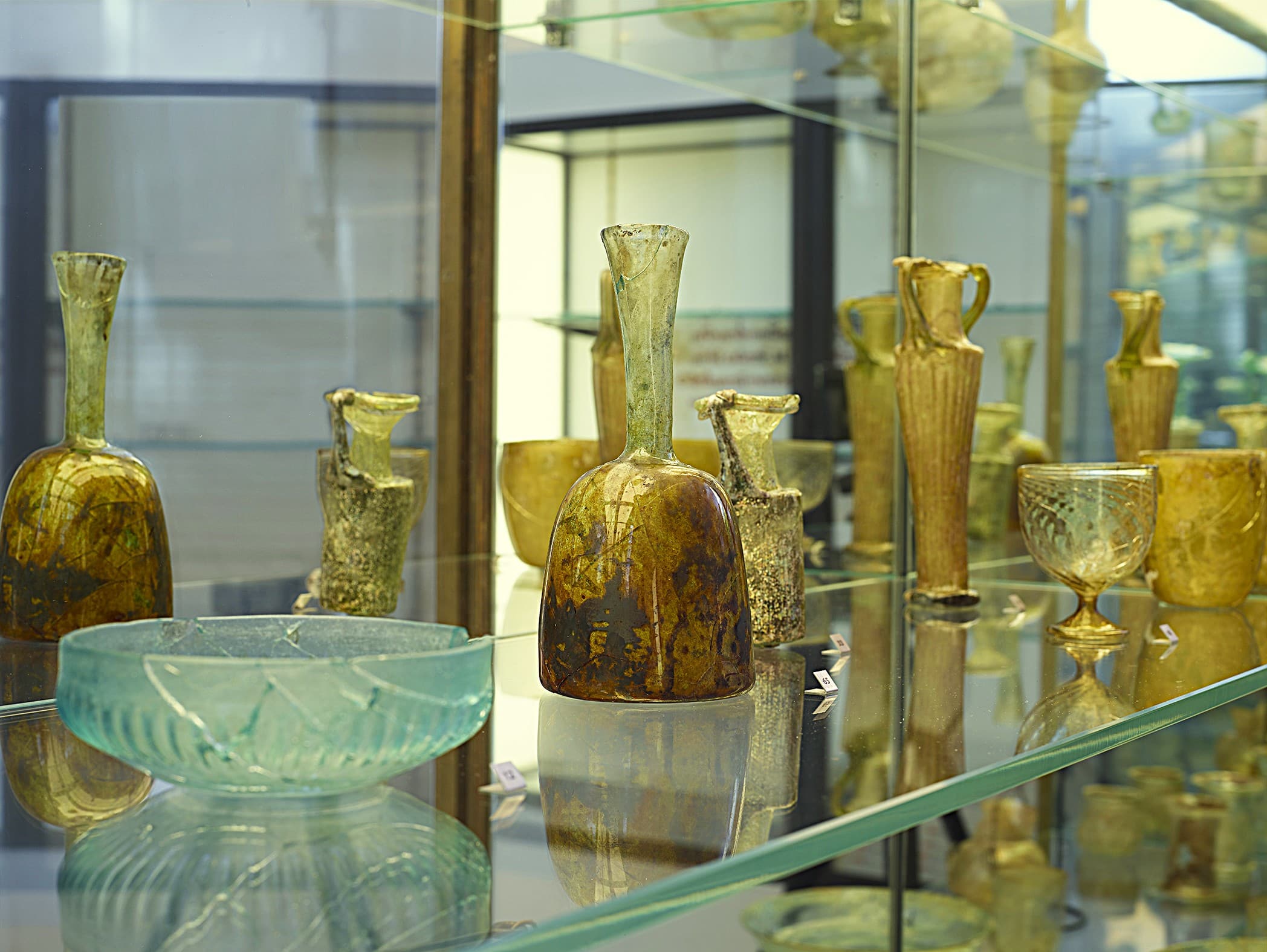 A brightly lit display of blue and brown glass vases and bowls. The glass objects sit on glass shelves and are encased in glass.