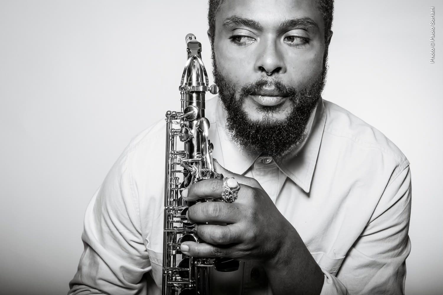 Black and white photo of Logan Richardson holding a saxophone and wearing a long sleeve, buttoned shirt.