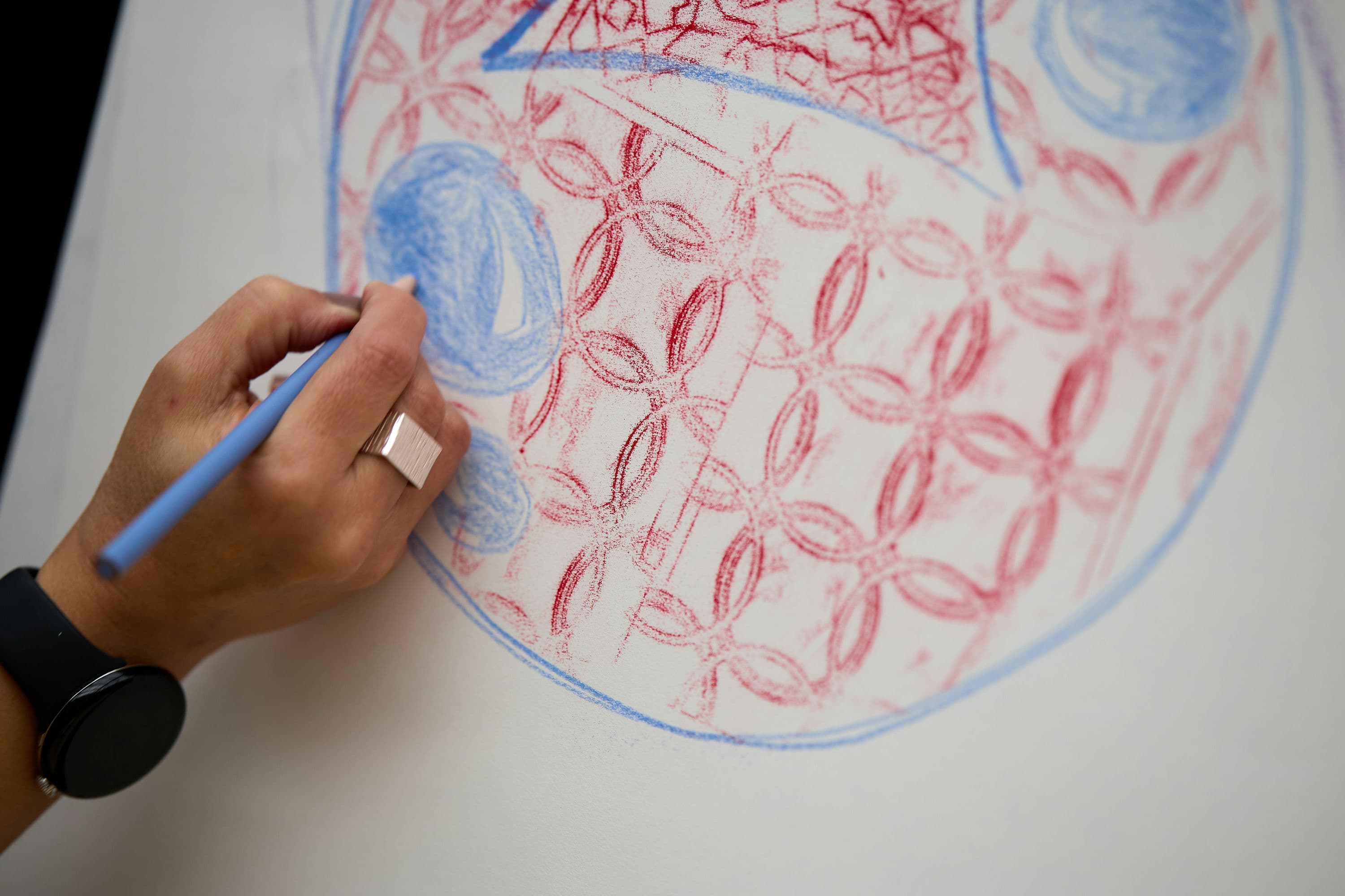 Hand drawing geometric shapes on paper with blue and red colored pencils.