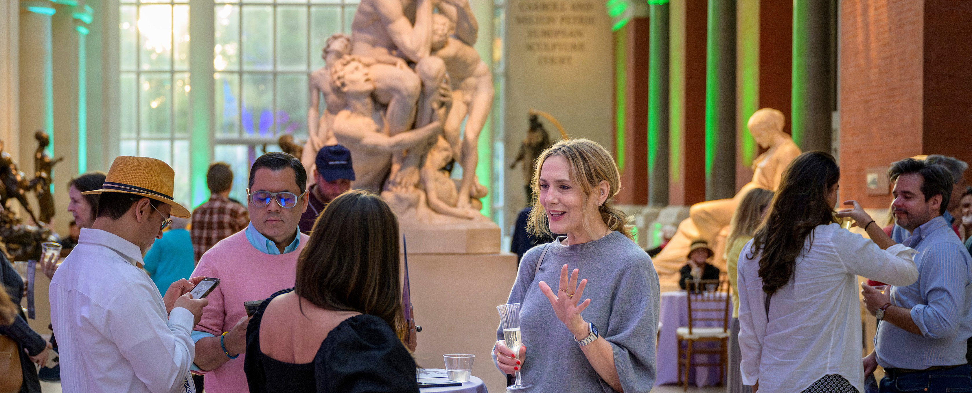 Small groups of Members conversing and enjoying drinks at The Met After Hours in The Carroll and Milton Petrie European Sculpture Court