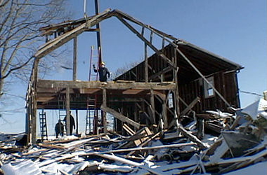 Video still of the frame of a house as it is being dismantled.