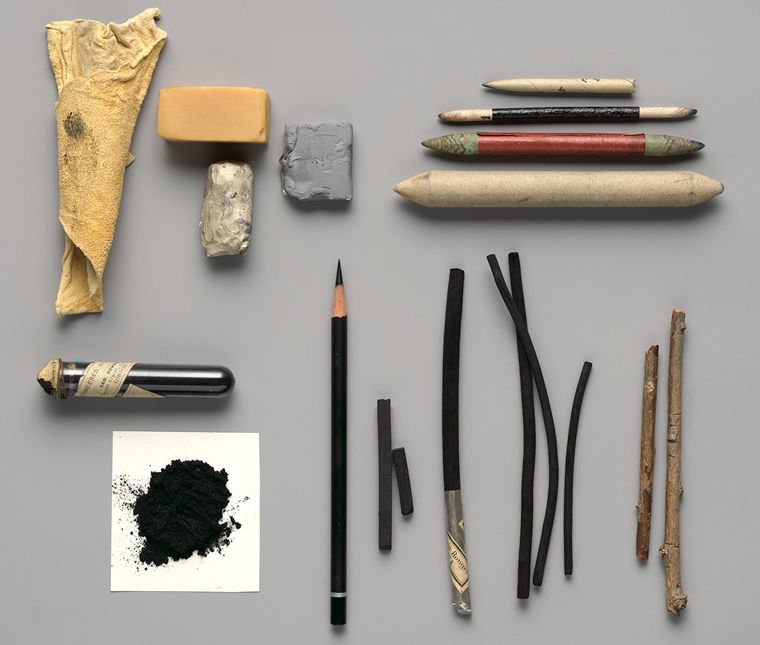 An artful arrangement of pencils, charcoal sticks, erasers, twigs, and other tools for charcoal drawing.
