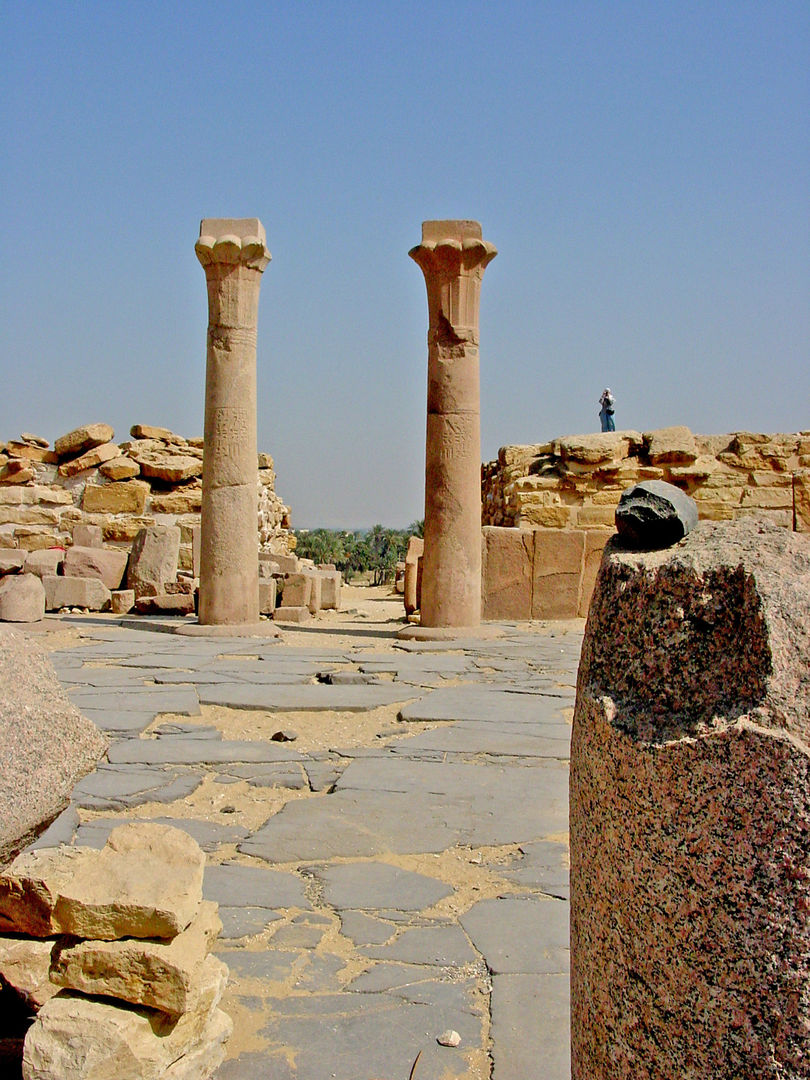 Color photo showing a pavement of grey stone, with two columns standing in the background.