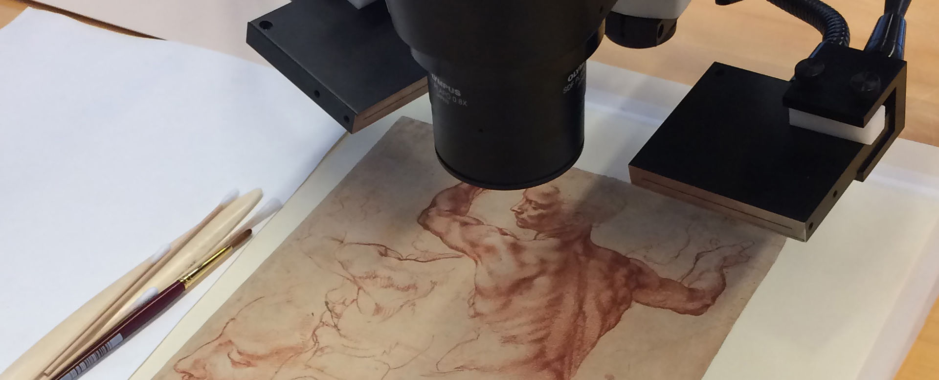 A Michelangelo drawing under a microscope with paintbrushes to its left