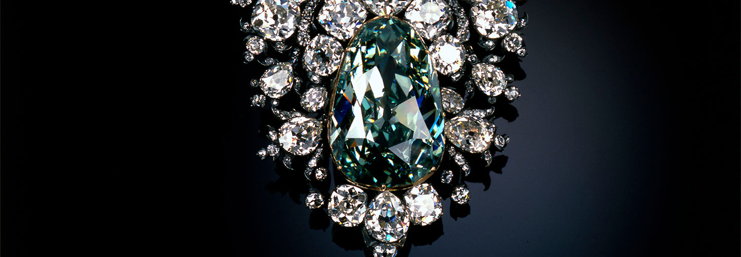A massive green diamond, cut in a pear shape and set in an ornate silver and diamond ornament