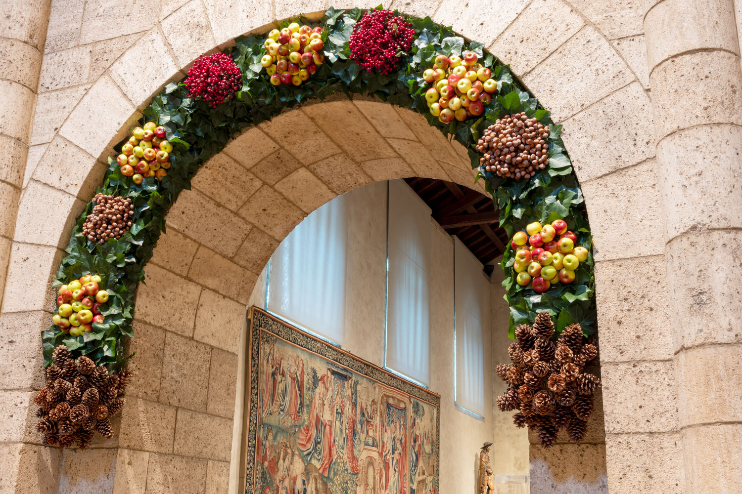 A festive wreath of holly and apples adorns a medieval arch at The Met Cloisters.