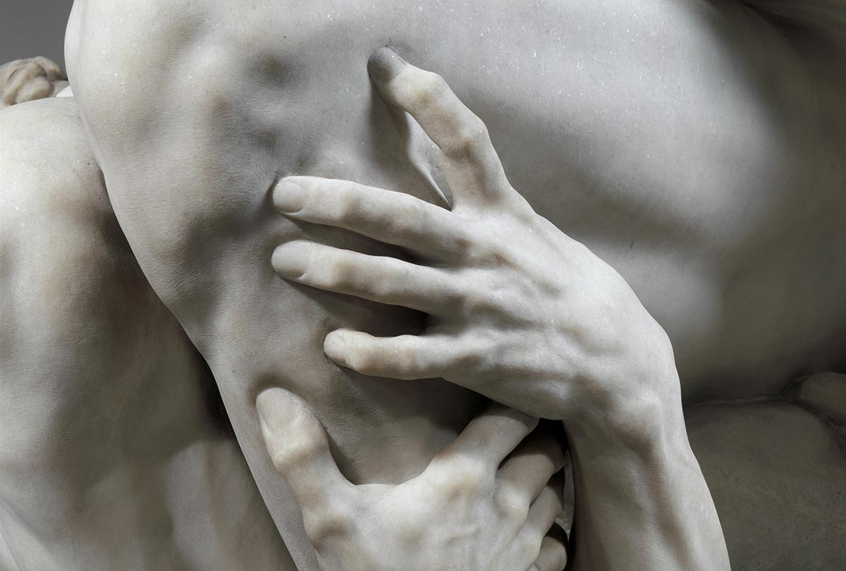 Detail of a marble sculpture with two hands grasping onto a man's leg