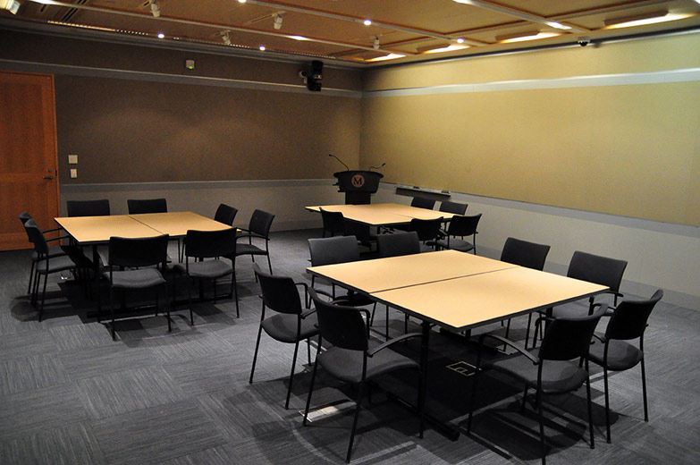 A small, comfortable, modern, carpeted room with gray fabricwalls and gray paneling; the room is set with three groupings tables with chairs