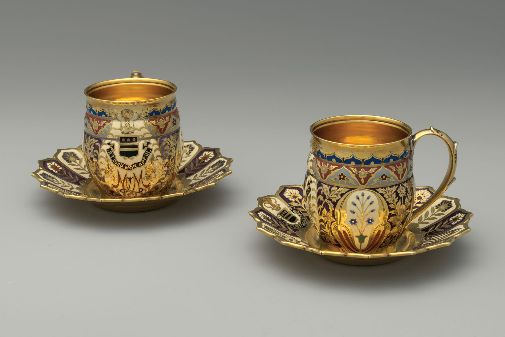 A pair of dazzling gilded and enameled cups and saucers adorned with floral designs, a coat of arms, and monogram