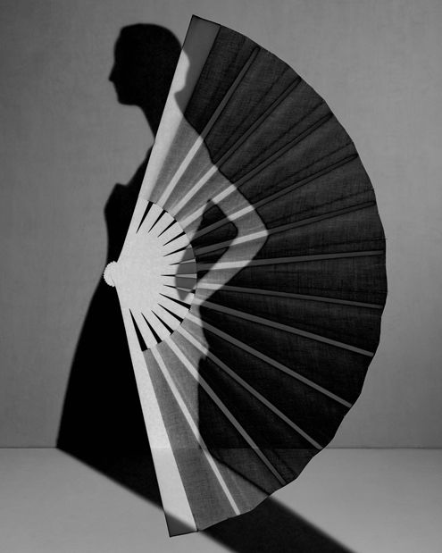 A black and white collage featuring a woman's silhouette in a dress overlayed on top of a folded fan 