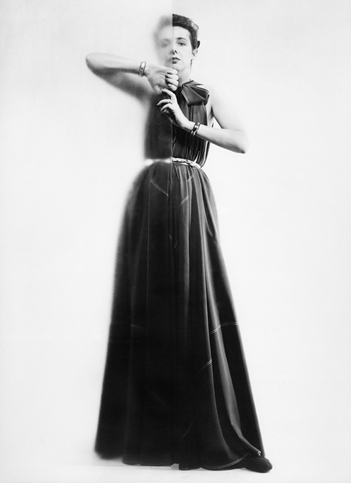A photograph of a woman in a long gown with her hands around a large glass wall down the center of her body