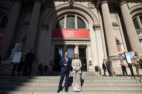 A man and woman in suits stand on the steps of a large building with a banner saying "The Met" above them