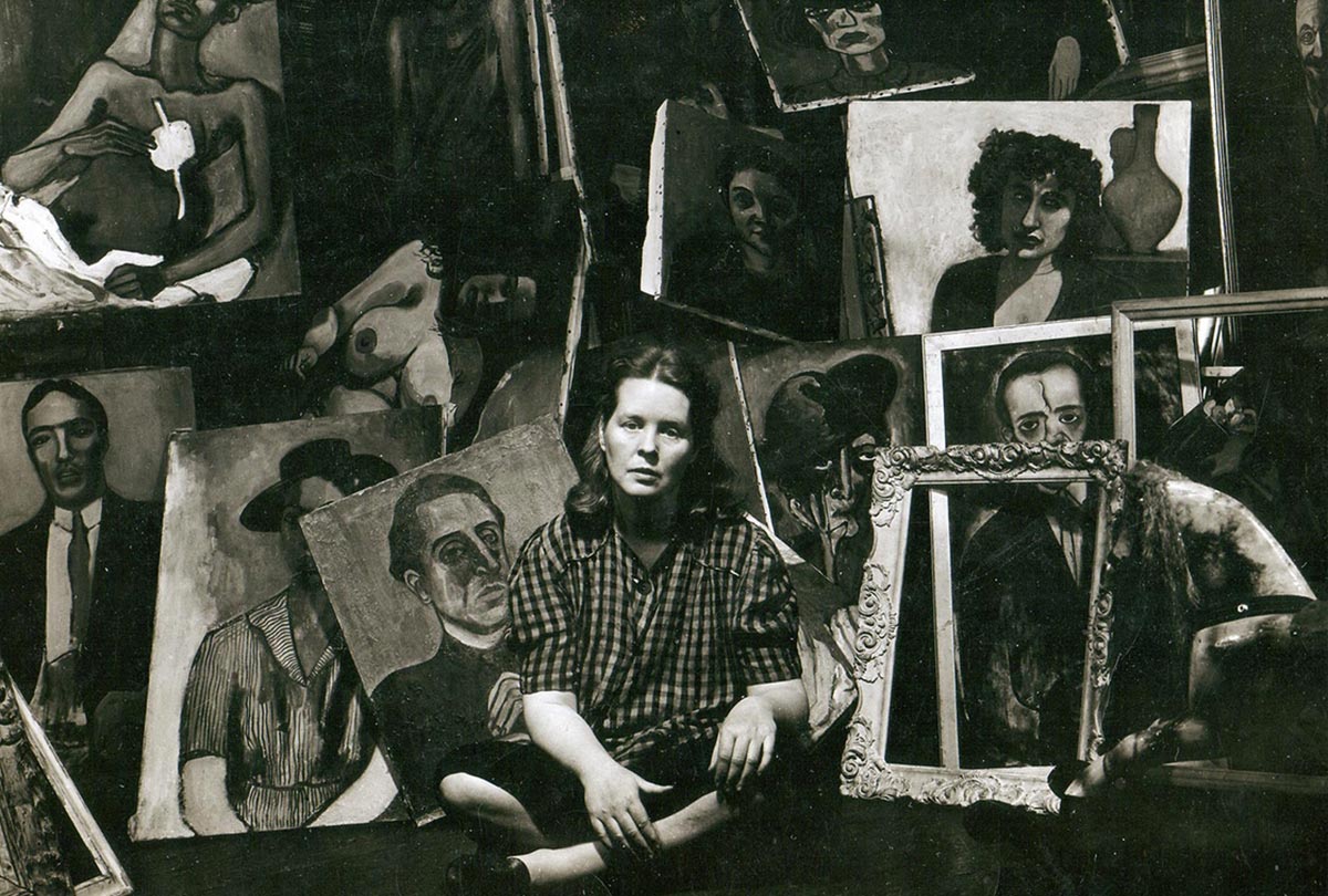 A woman sits on the floor among a series of portraits