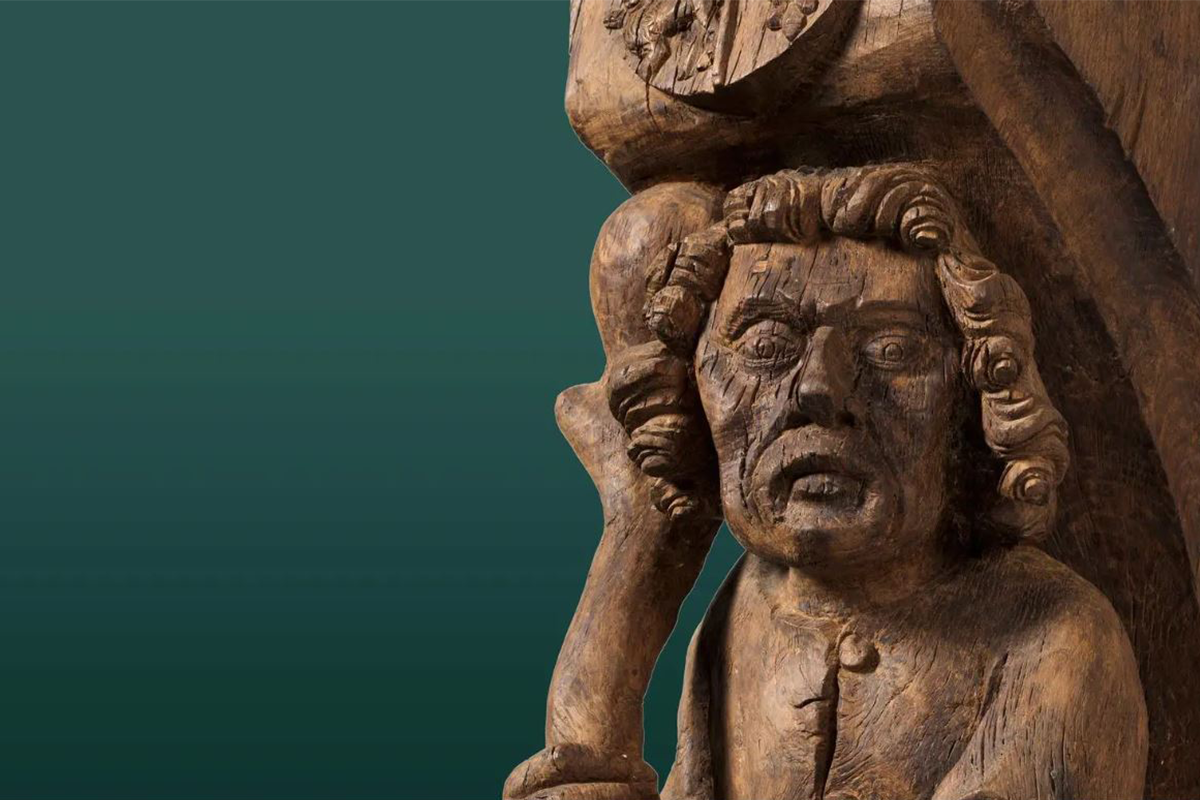 A medieval wooden sculpture of a man against an emerald green background.