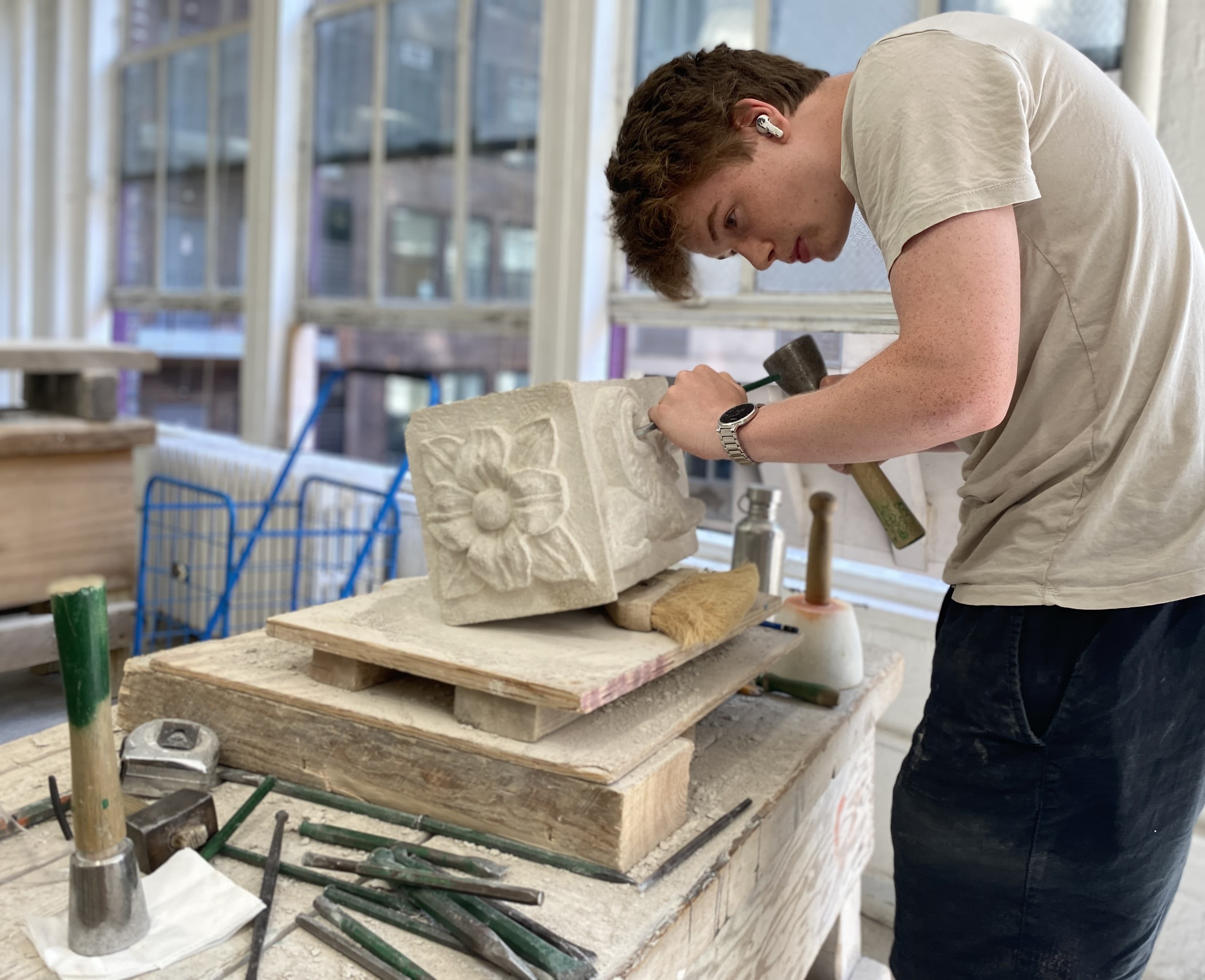 A young person sculpting stone with a mallet and chisel