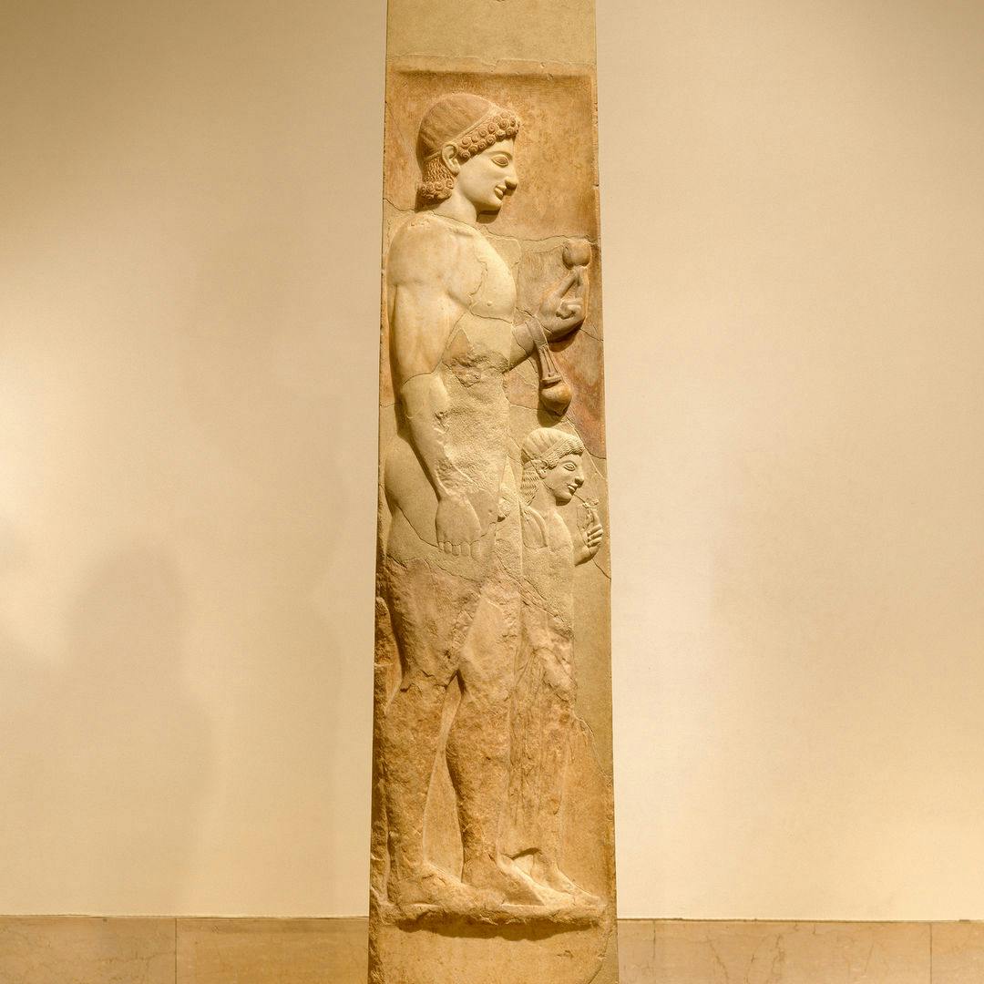 Marble stele from ancient Greece. The shaft depicts a young, athletic man holding a pomegranate and oil flask. His little sister is next to him, holding a flower.