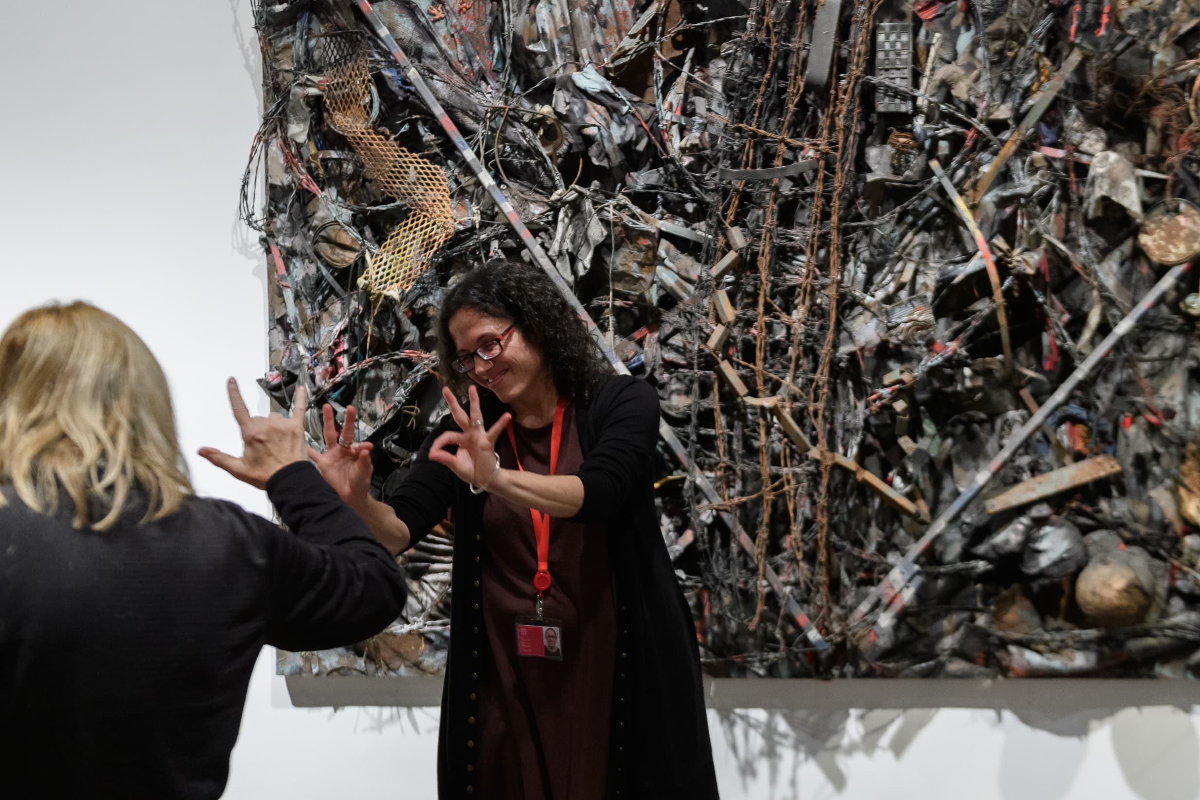 A Met educator signs “okay” to an audience as she stands in front of an artwork. On the left, there is a person with their back to the camera signing “I love.”
