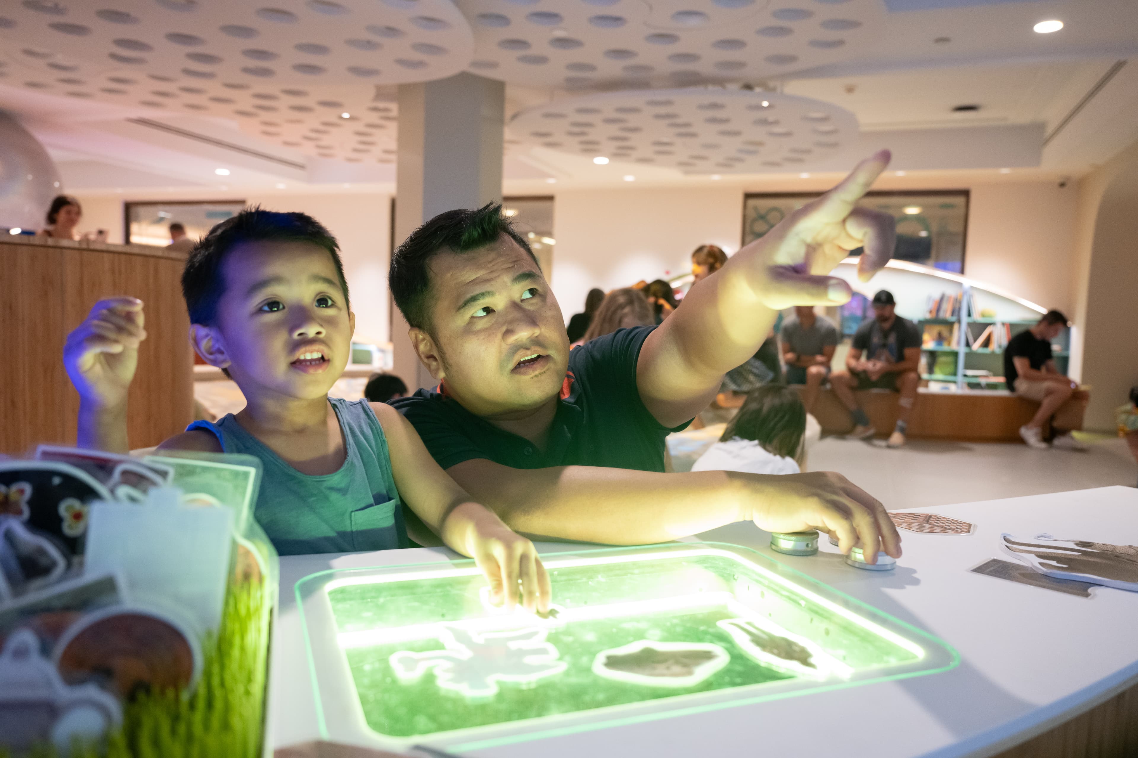 A child and caregiver explore storytelling through different forms of art, lights, and sounds. The caregiver points to something out of frame, and the child plays with a green light board.